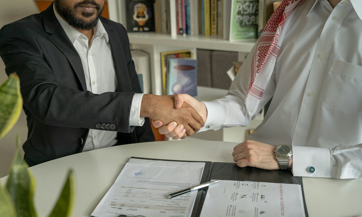 A handshake over a signed document. Each person at the table has their own reason to be careful.