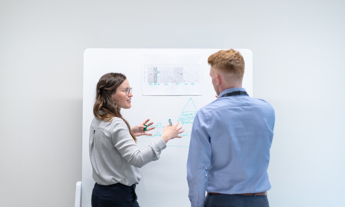 Twee collega's die iets uitwerken op een whiteboard. Uren van je eigen mensen zijn de kostenpost die nooit in een offerte staat.