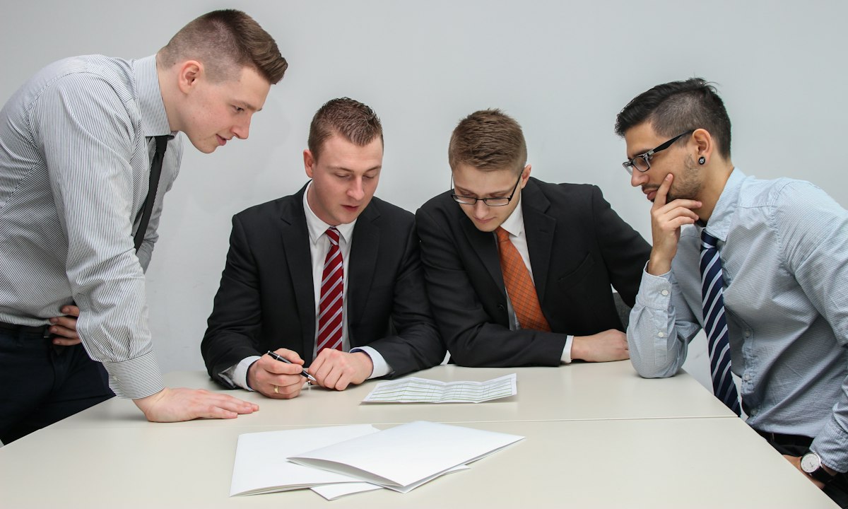 Vier mensen buigen zich over een document op tafel. Een directie leert door de echte besluiten zelf te nemen.