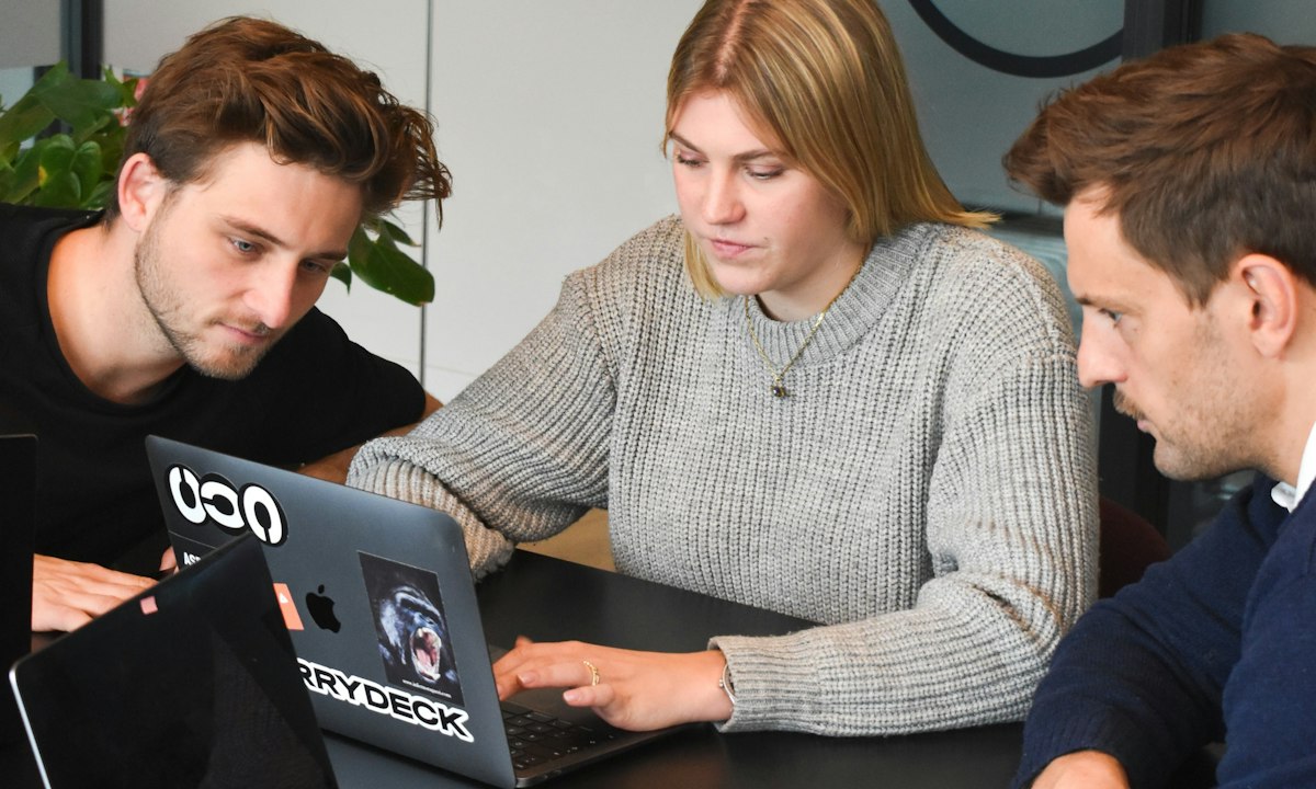 Drie collega's werken samen aan een laptop. Doeners leren door te bouwen, met een tweede persoon die ook weet hoe het werkt.